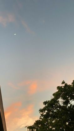 an airplane flying in the sky over some trees and buildings at sunset or dawn with a half moon behind it