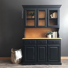 a black hutch with books and plants in it next to a wicker basket