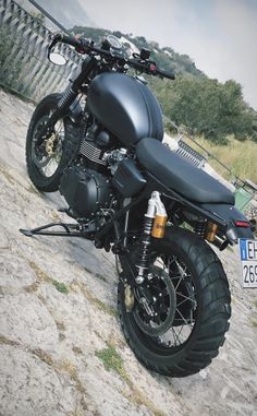 a black motorcycle parked on top of a stone road next to a wooden fence and grass