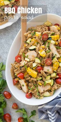 a white bowl filled with pasta salad next to a wooden spoon and some tomatoes on the side