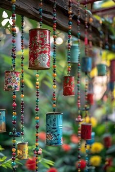 colorful tin can wind chimes hanging from a wooden beam in a garden filled with flowers