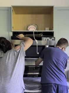 two people are working on an oven in the kitchen with their backs turned to look like they're trying to fix it