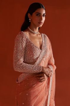 a woman in an orange sari poses for the camera with her hands on her hips