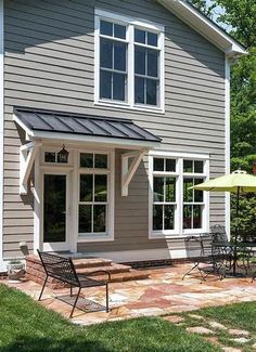 a gray house with an umbrella and chairs in the front yard, on a sunny day