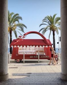 a woman standing in front of a red car on the street next to palm trees