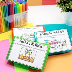 three cards with words and pictures on them sitting next to colored pencils in front of a potted plant