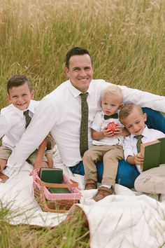 a man and two boys are sitting on a blanket in the grass with an open book