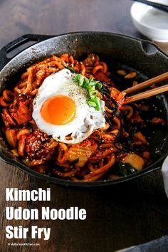 a skillet filled with noodles and an egg on top, next to chopsticks