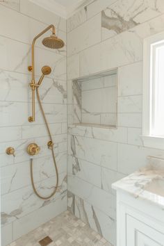 a bathroom with marble tile and gold shower faucet next to a white sink