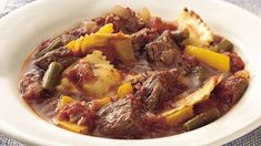 a white bowl filled with stew and potatoes on top of a table cloth next to a fork