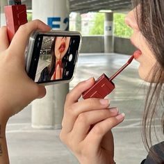 a woman taking a selfie with her cell phone and lipstick in the other hand