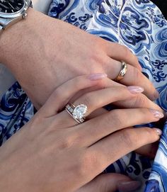 two hands holding onto each other while wearing matching wedding bands and engagement rings on their fingers