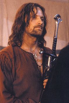 a man with long hair holding a large metal object in his right hand and looking off into the distance