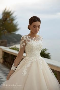 a woman in a wedding dress is standing on a balcony near the water and looking down at her hand