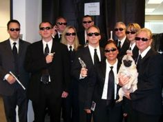 a group of people in suits and sunglasses posing for a photo with a pug