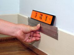 a person is holding a piece of wood with an orange clock on the wall behind them