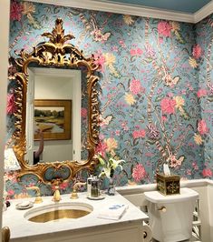 a bathroom with blue and pink wallpaper, gold framed mirror, toilet and sink