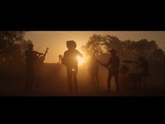 the silhouettes of people playing instruments in front of an orange light at sunset with trees