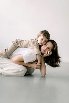 a woman holding a small child on her back while posing for a photo in front of a white wall