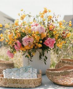 a white vase filled with lots of flowers on top of a table next to baskets