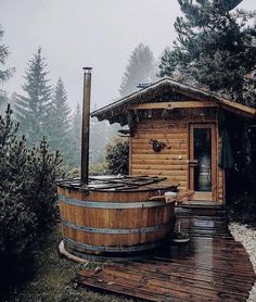 a wooden hot tub sitting on top of a wooden deck next to a tree filled forest