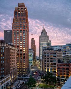 the city skyline is lit up at dusk with skyscrapers in the background and cars parked on the street