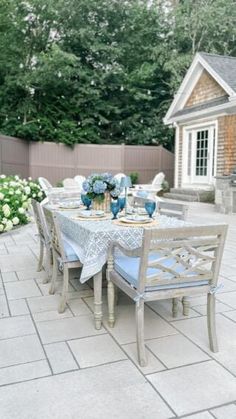 an outdoor dining table with blue vases and flowers on it in front of a house