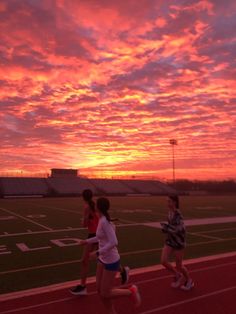 three girls running on a track at sunset