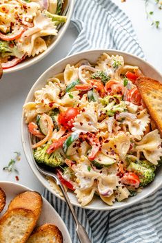 two bowls filled with pasta and vegetables next to garlic bread