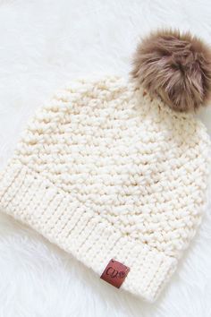 a white knitted hat with a brown pom - pom on the top