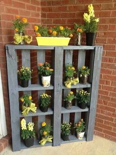 a wooden shelf filled with potted plants on the side of a brick wall next to a door