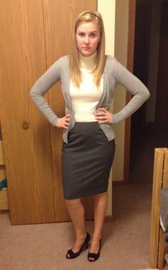 a woman standing in front of a wooden door wearing a skirt and cardigan sweater