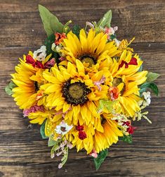 a bouquet of sunflowers and other flowers on top of a wooden table with leaves