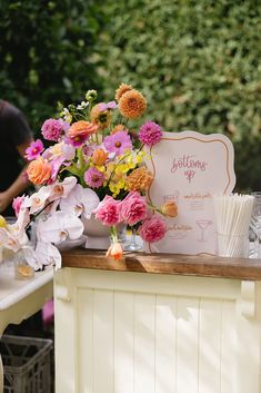 a table topped with lots of flowers next to a white sign that says blossoming up