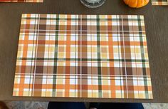 an orange plaid table cloth on top of a wooden table next to some pumpkins