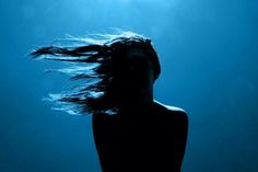 a woman's hair is blowing in the wind under blue water with sunbeams