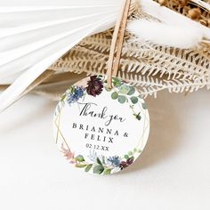 a wedding thank tag with flowers and leaves on it sitting in front of some feathers