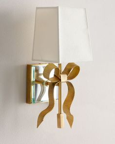 a wall light with a white shade on it and a gold bow around the lamp