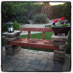 a wooden bench sitting next to a potted plant on top of a brick walkway