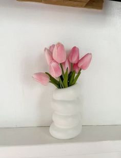 a white vase filled with pink tulips on top of a shelf next to a wall