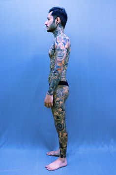 a man with tattoos on his body standing in front of a blue background