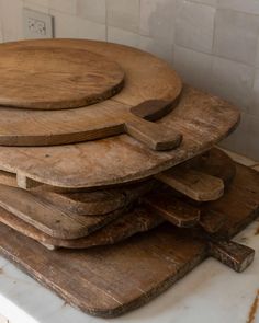 a stack of wooden cutting boards sitting on top of a white counter next to a tiled wall