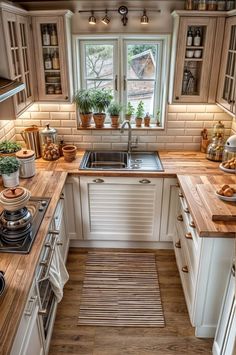 a kitchen with wooden counter tops and white cabinets, along with potted plants on the window sill