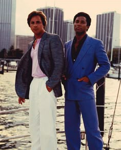 two men standing on the deck of a boat in front of some buildings and water