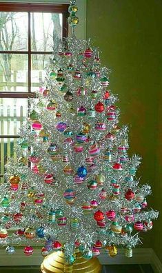 a white christmas tree sitting in front of a window with ornaments on top of it