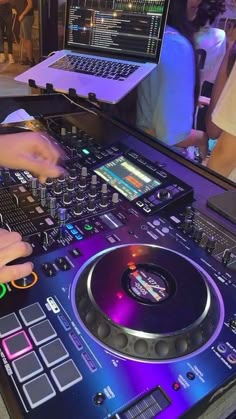 a dj mixing music in front of a laptop on a table with other people behind it