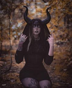 a woman with horns on her head sitting in the woods