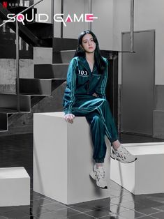 a woman sitting on top of a white block wearing a green suit and matching sneakers