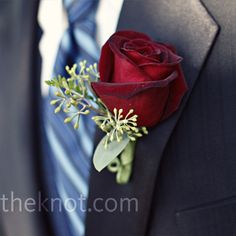 a boutonniere with a single red rose attached to the lapel of a suit