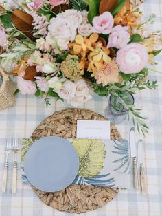 a place setting with flowers and plates on the table cloth, along with silverware